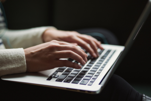 Two hands of a Caucasian woman typing on a laptop