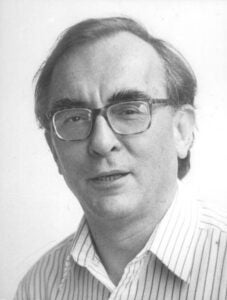 Imagen en blanco y negro de un hombre de mediana edad con gafas y camisa a rays mirando a la cámara