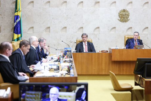 Justices of the Brazilian Supreme Court (STF) participate in a plenary session. One justice sits at the center of the image, while other members of the court are seated to the left, engaged in discussion.