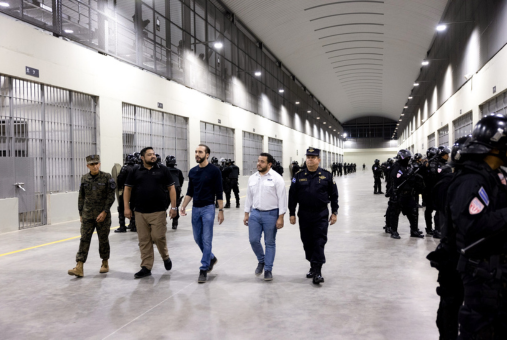President Nayib Bukele walks with top security and government officials inside El Salvador’s high-security Terrorism Confinement Center (CECOT), flanked by rows of heavily armed police officers.